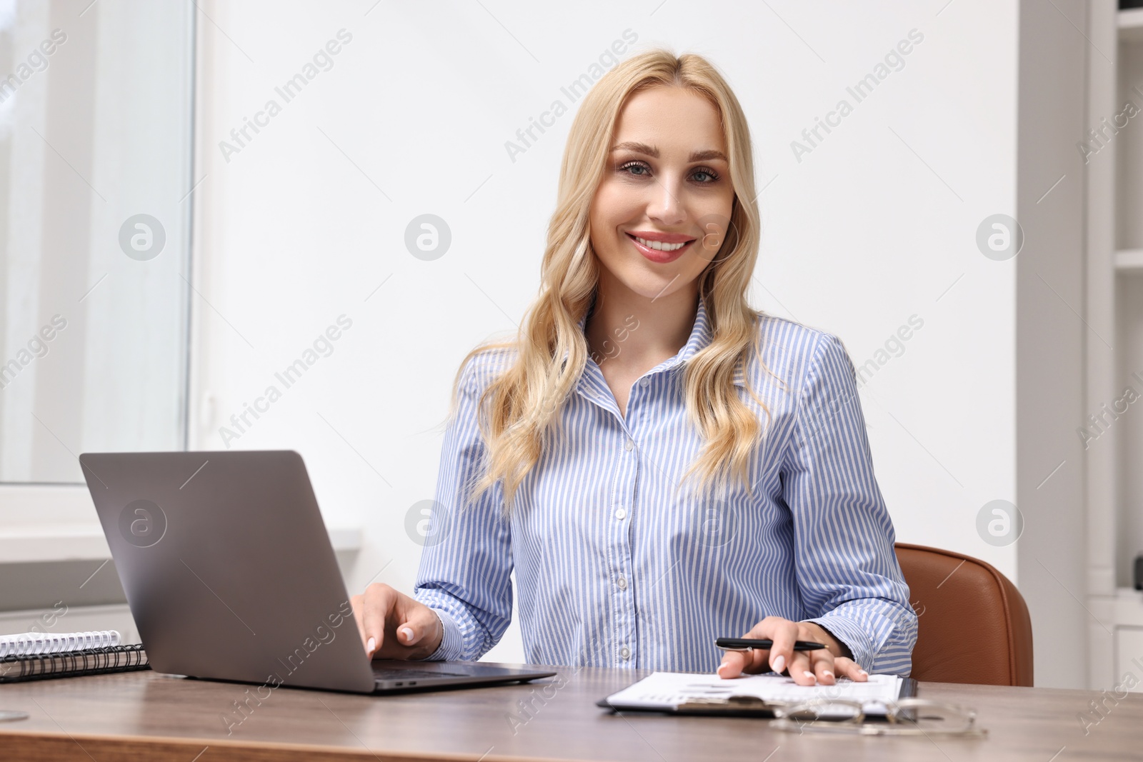 Photo of Happy secretary at table with laptop and stationery in office