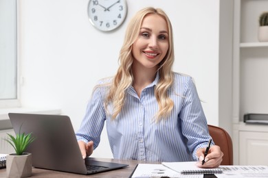 Happy secretary taking notes at table in office