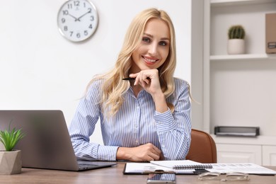 Happy secretary with pen at table in office