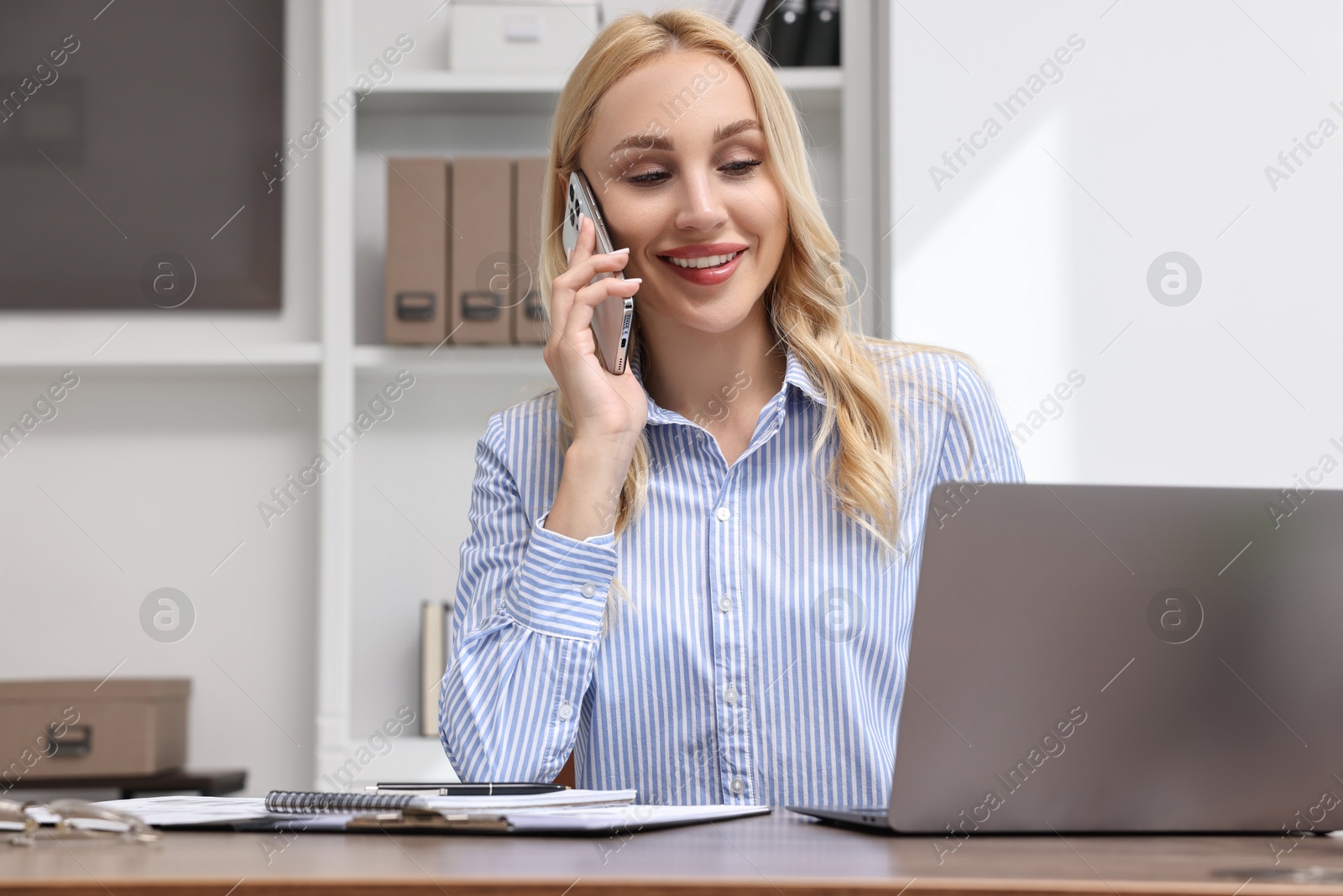 Photo of Happy secretary talking on smartphone at table in office