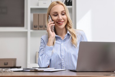 Happy secretary talking on smartphone at table in office