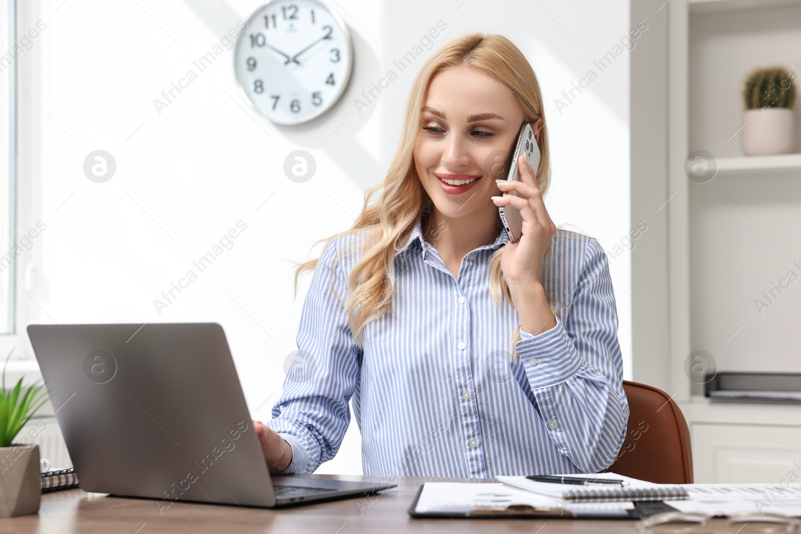 Photo of Happy secretary talking on smartphone at table in office