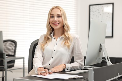 Photo of Happy secretary with pen at table in office