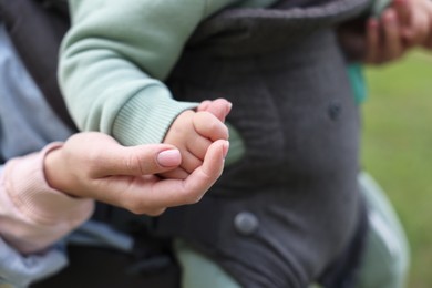 Photo of Mother holding her child in sling (baby carrier) on blurred background, closeup