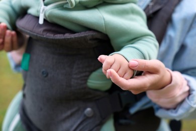 Photo of Mother holding her child in sling (baby carrier) on blurred background, closeup