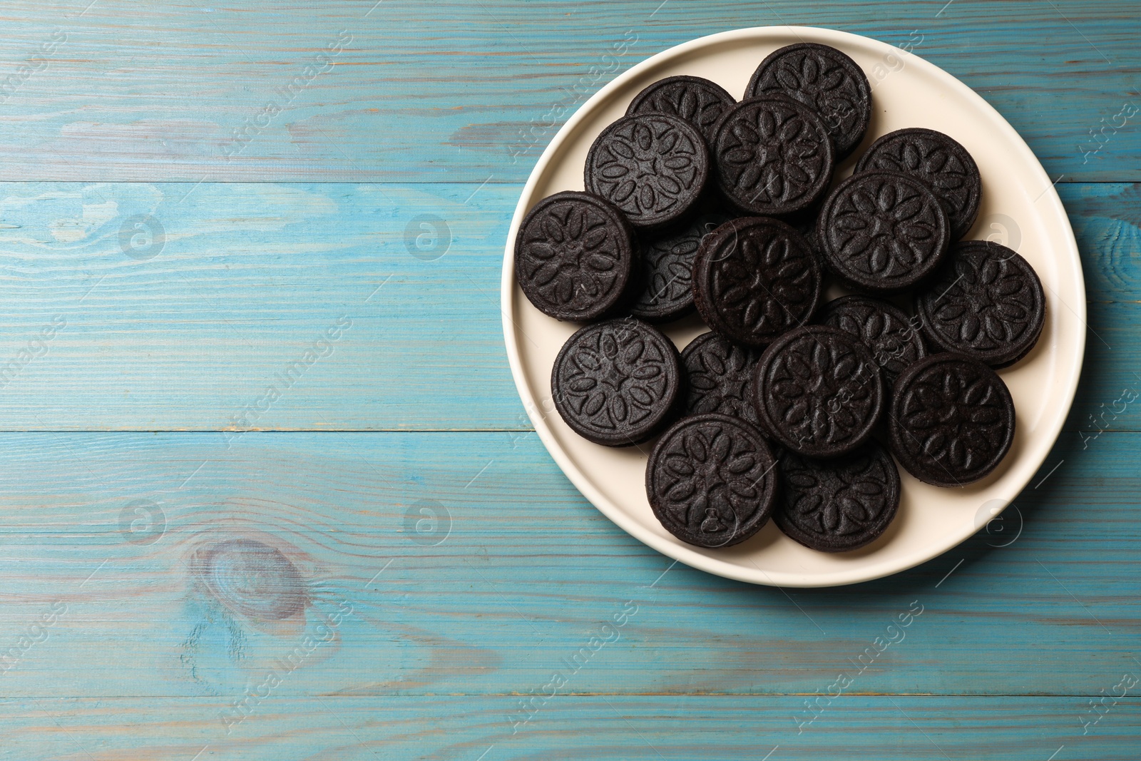 Photo of Plate with tasty sandwich cookies on light blue wooden table, top view. Space for text