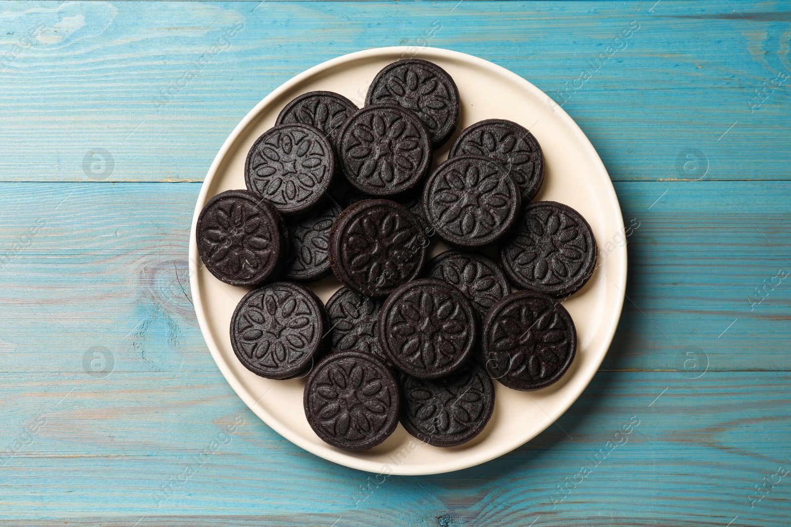 Photo of Plate with tasty sandwich cookies on light blue wooden table, top view