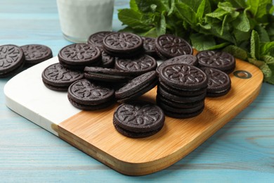 Photo of Board with tasty sandwich cookies and mint on light blue wooden table, closeup