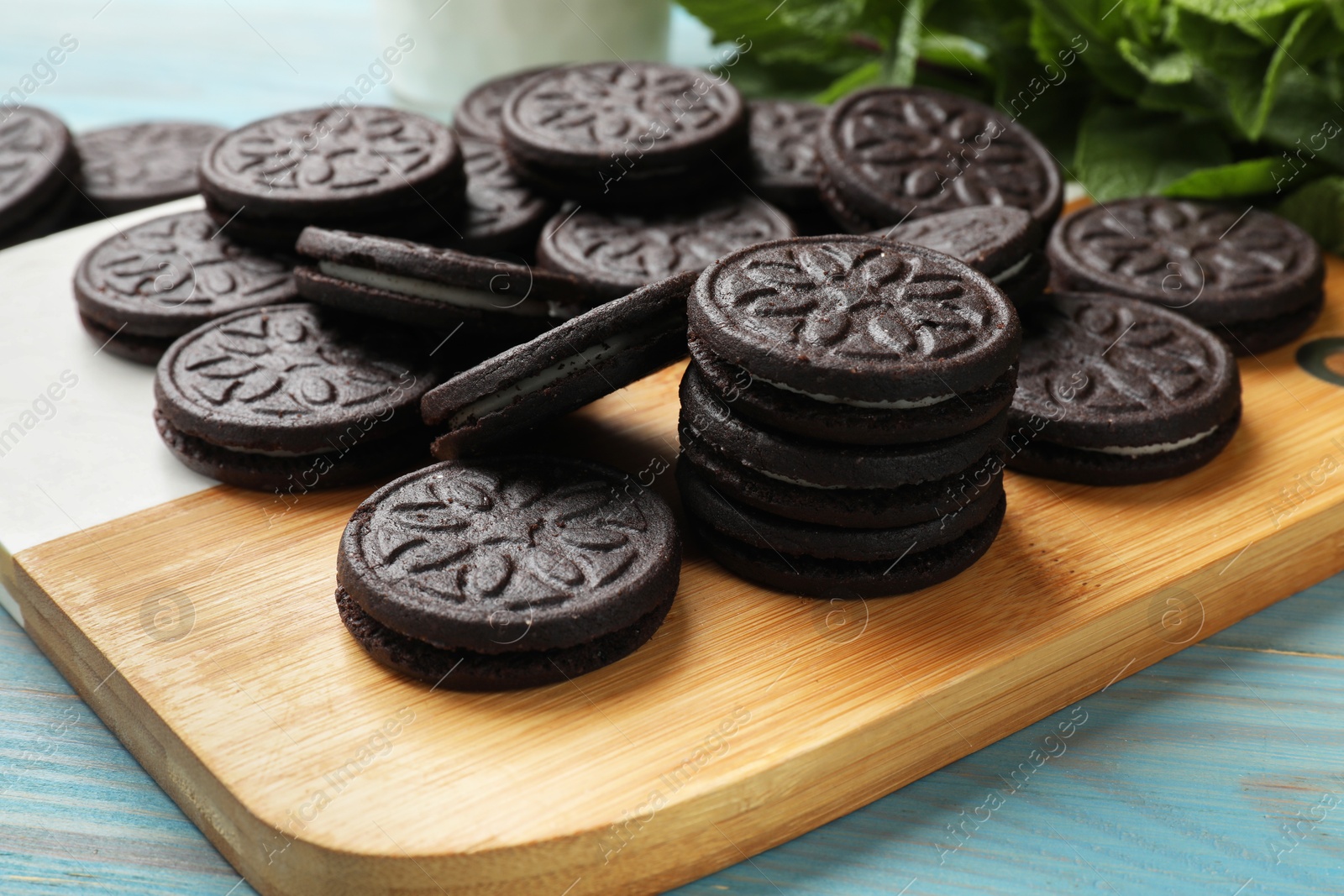 Photo of Board with tasty sandwich cookies on light blue wooden table, closeup