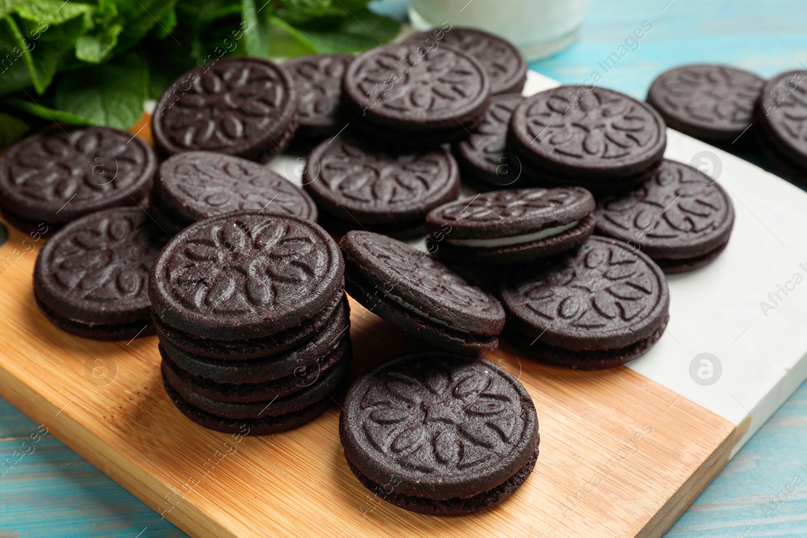 Photo of Board with tasty sandwich cookies on light blue wooden table, closeup