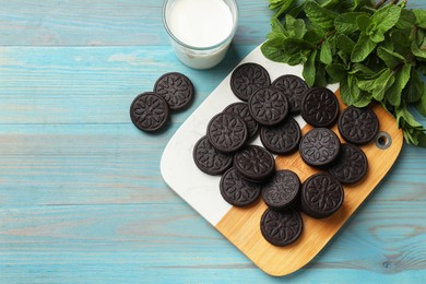 Board with tasty sandwich cookies and mint on light blue wooden table, flat lay. Space for text