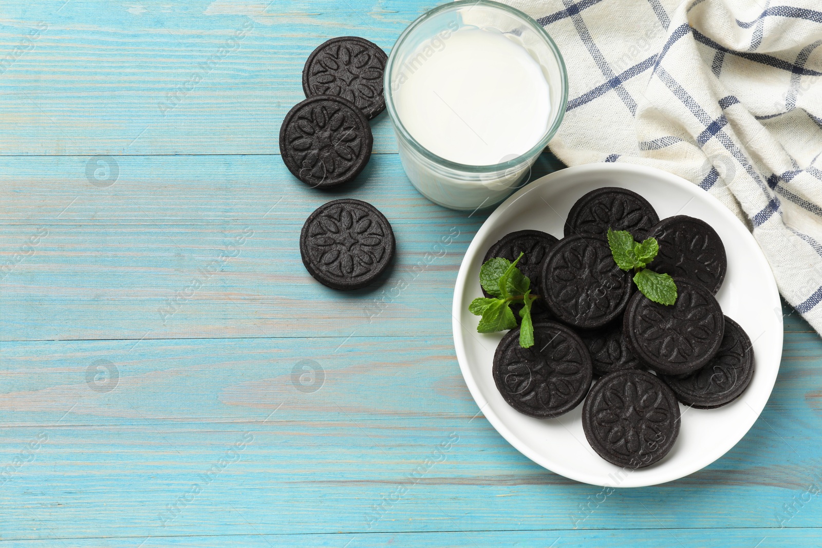 Photo of Plate with tasty sandwich cookies, mint and glass of milk on light blue wooden table, flat lay. Space for text