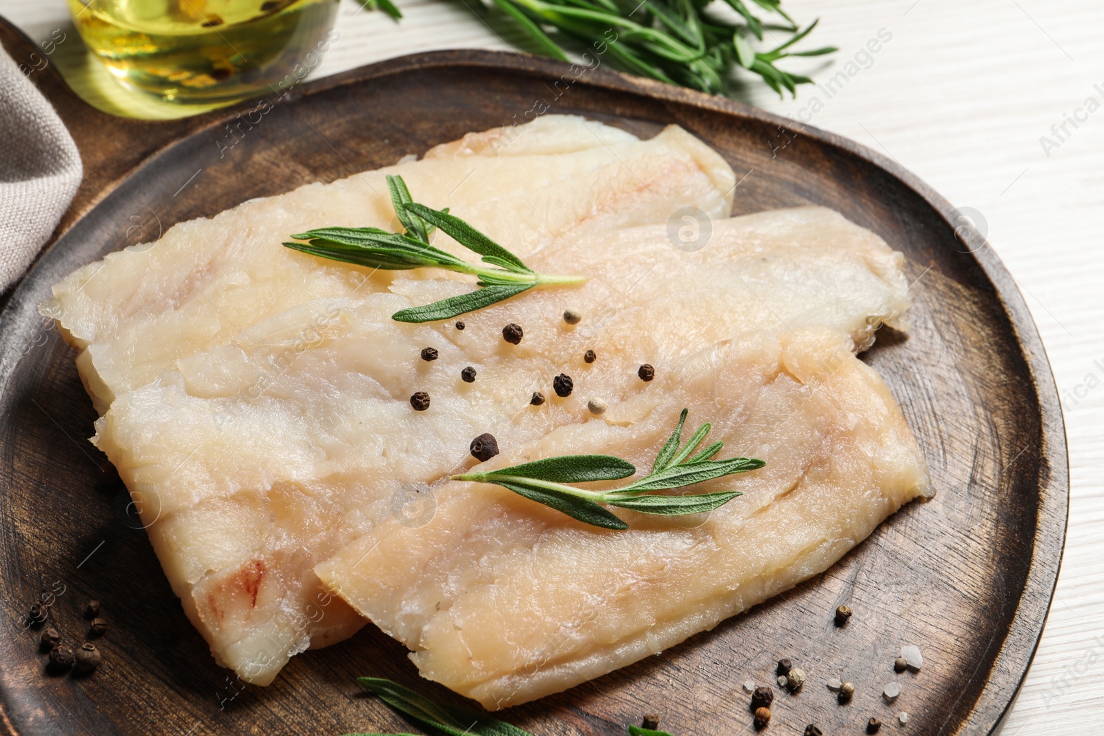 Photo of Raw cod fish, rosemary and spices on white wooden table, closeup