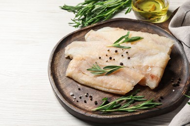 Photo of Raw cod fish, rosemary and spices on white wooden table, closeup. Space for text