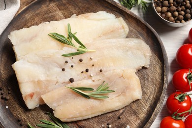 Photo of Raw cod fish, rosemary, tomatoes and spices on white wooden table, flat lay