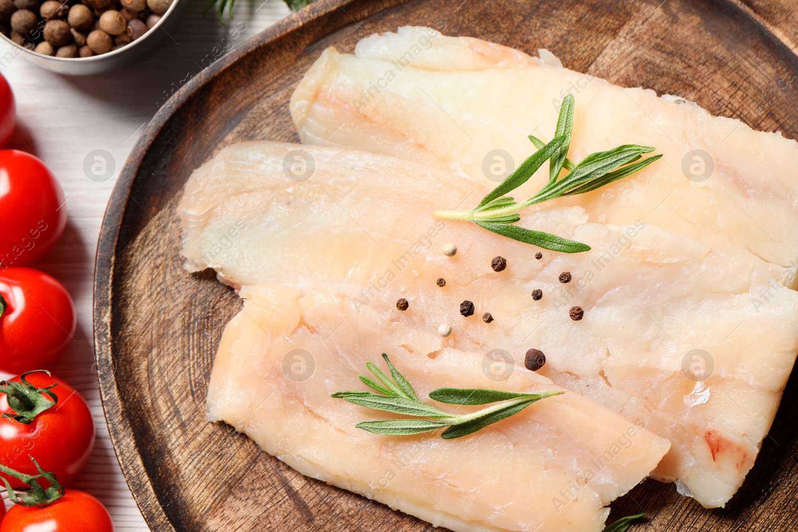 Photo of Raw cod fish, rosemary, tomatoes and spices on white wooden table, flat lay