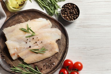 Raw cod fish, rosemary, tomatoes and spices on white wooden table, flat lay. Space for text