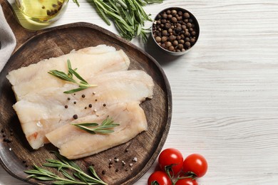 Photo of Raw cod fish, rosemary, tomatoes and spices on white wooden table, flat lay. Space for text