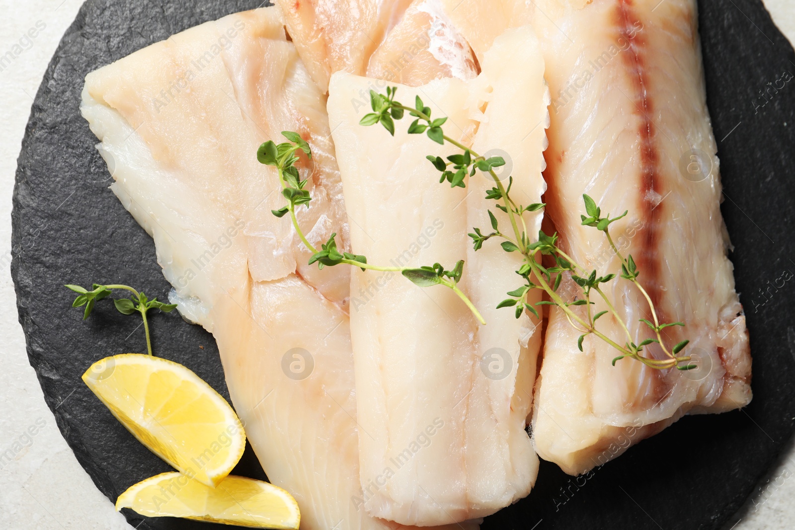 Photo of Pieces of raw cod fish and lemon on light grey table, top view