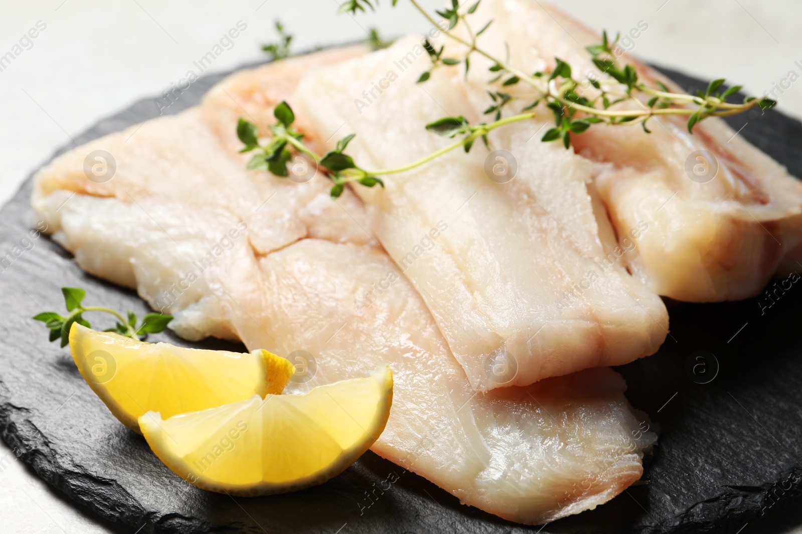 Photo of Pieces of raw cod fish and lemon on table, closeup