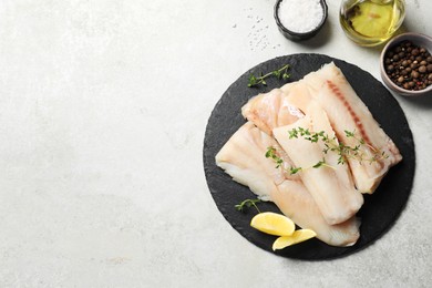 Pieces of raw cod fish, lemon and spices on light grey table, top view. Space for text