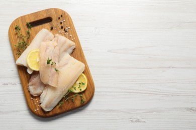 Photo of Pieces of raw cod fish, lemon and spices on white wooden table, top view. Space for text