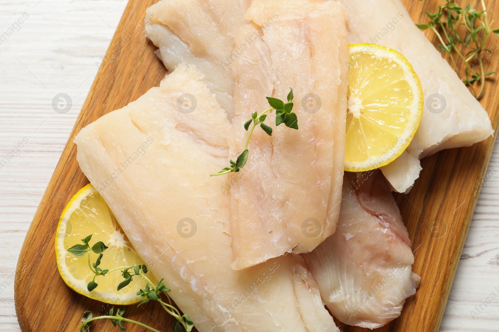 Photo of Pieces of raw cod fish, lemon and spices on white wooden table, top view