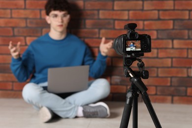 Photo of Teenage blogger explaining something while streaming indoors, focus on camera