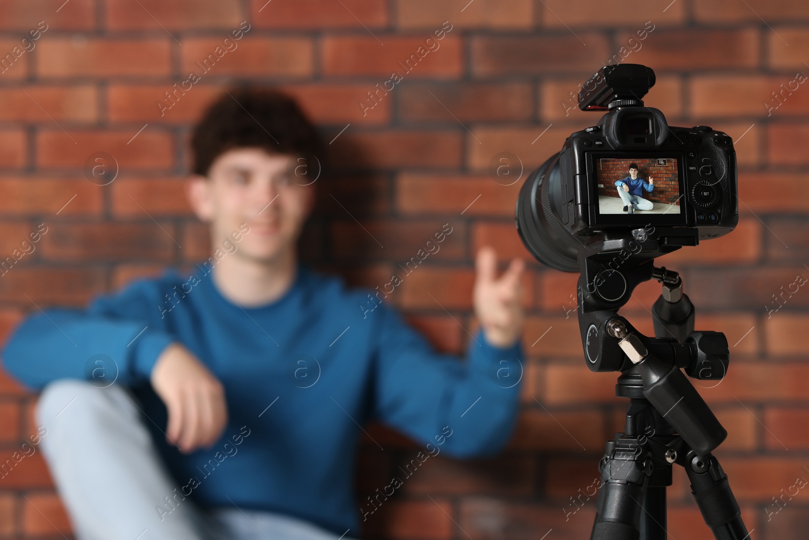 Photo of Teenage blogger explaining something while streaming indoors, focus on camera