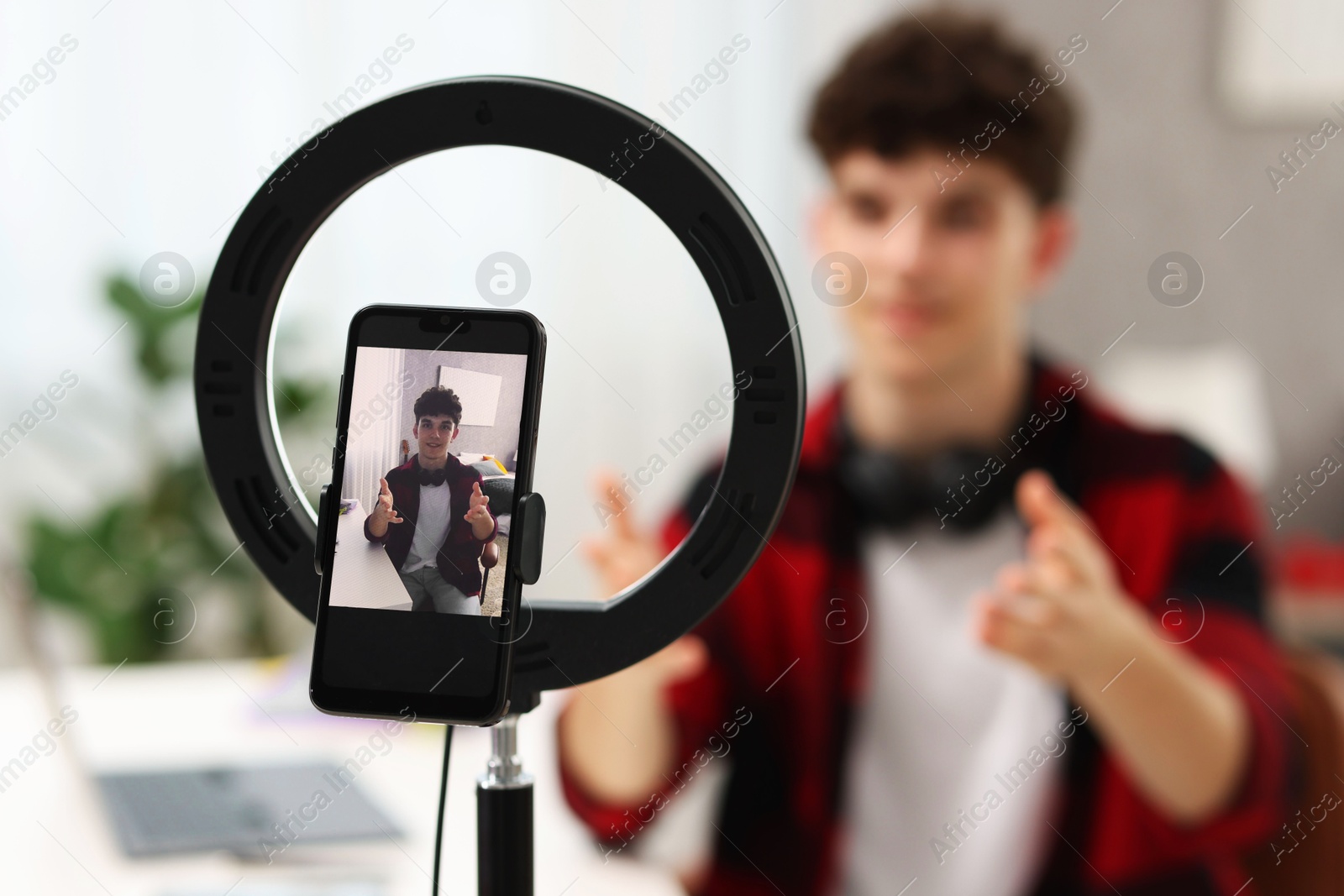 Photo of Teenage blogger explaining something while streaming at home, focus on smartphone