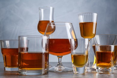 Photo of Different liqueurs in glasses on grey table, closeup