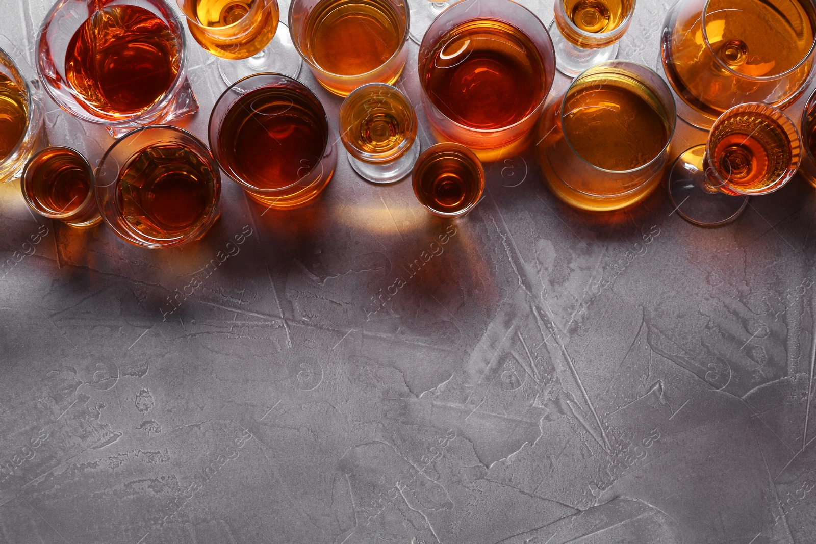 Photo of Many different liqueurs in glasses on grey textured table, flat lay. Space for text