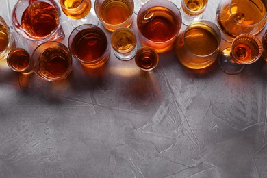 Photo of Many different liqueurs in glasses on grey textured table, flat lay. Space for text