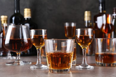 Many different liqueurs in glasses on grey textured table, closeup