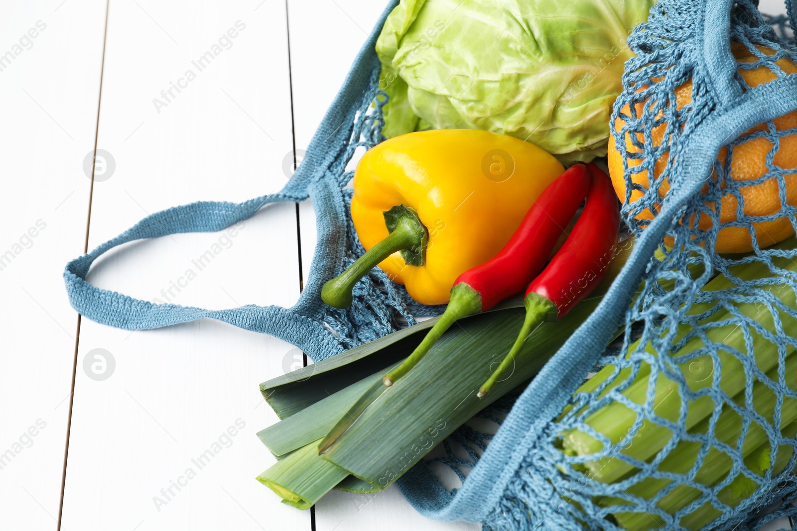 Photo of String bag with different vegetables on white wooden table, closeup