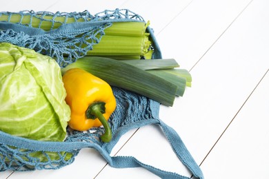 Photo of String bag with different vegetables on white wooden table, closeup. Space for text