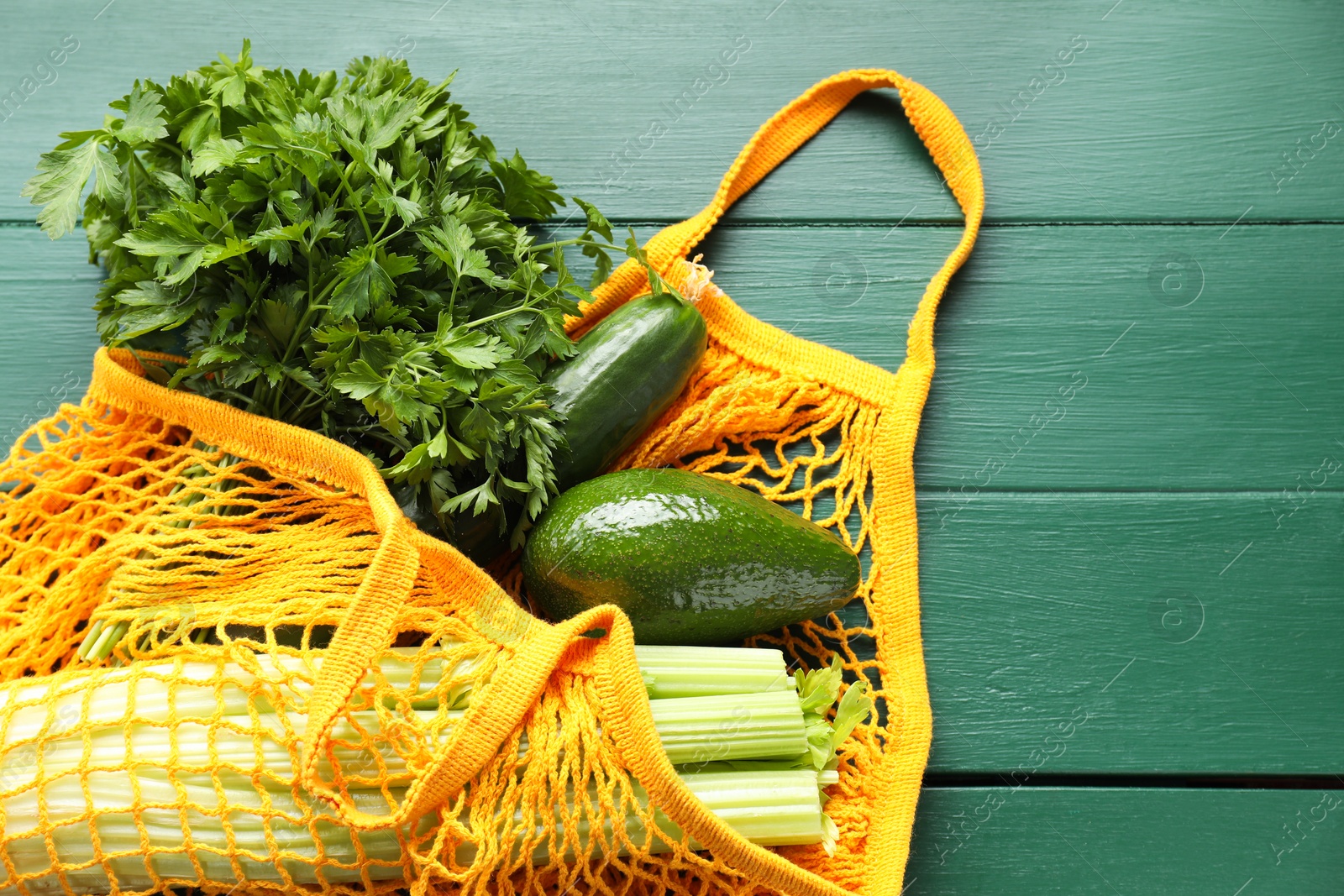 Photo of String bag with different vegetables on green wooden table, top view