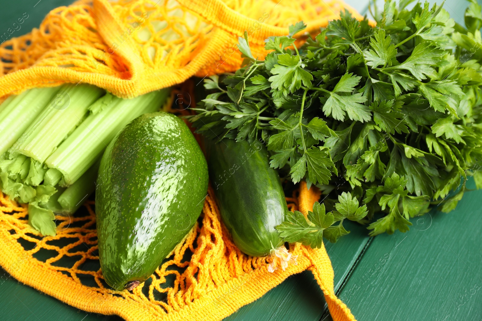 Photo of String bag with different vegetables on green wooden table, closeup