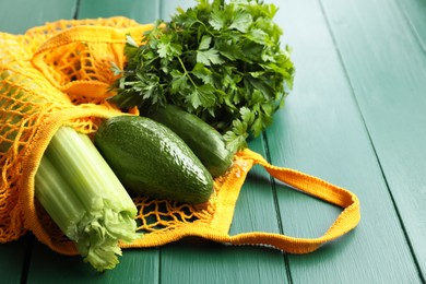 Photo of String bag with different vegetables on green wooden table, closeup