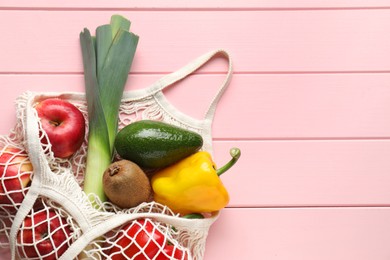 Photo of String bag with different vegetables and fruits on pink wooden table, top view. Space for text