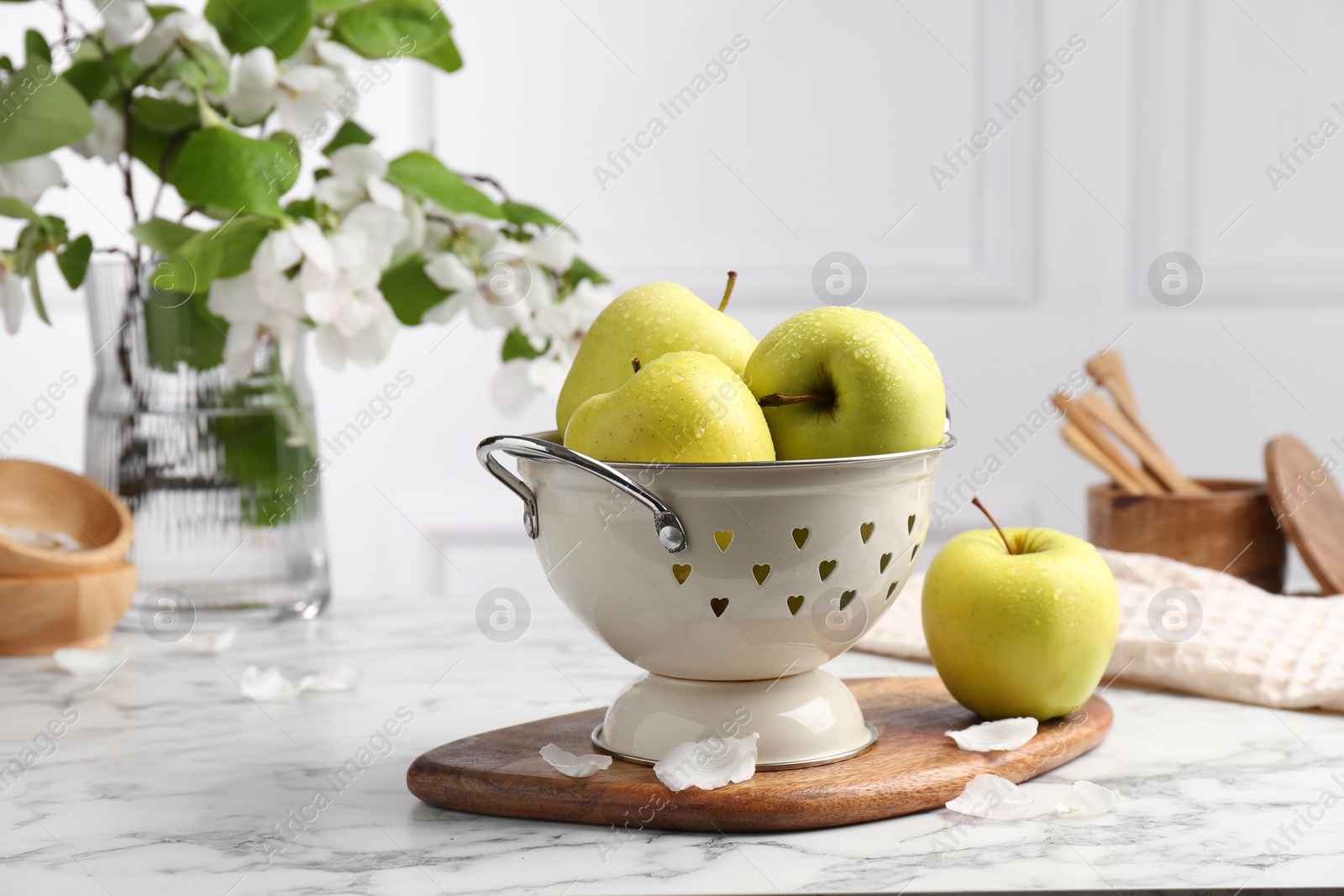 Photo of Colander with fresh apples and flower petals on white marble table