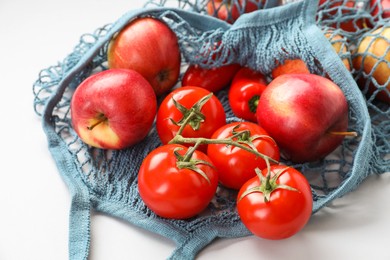 Photo of String bag with vegetables and apples on light grey background, closeup