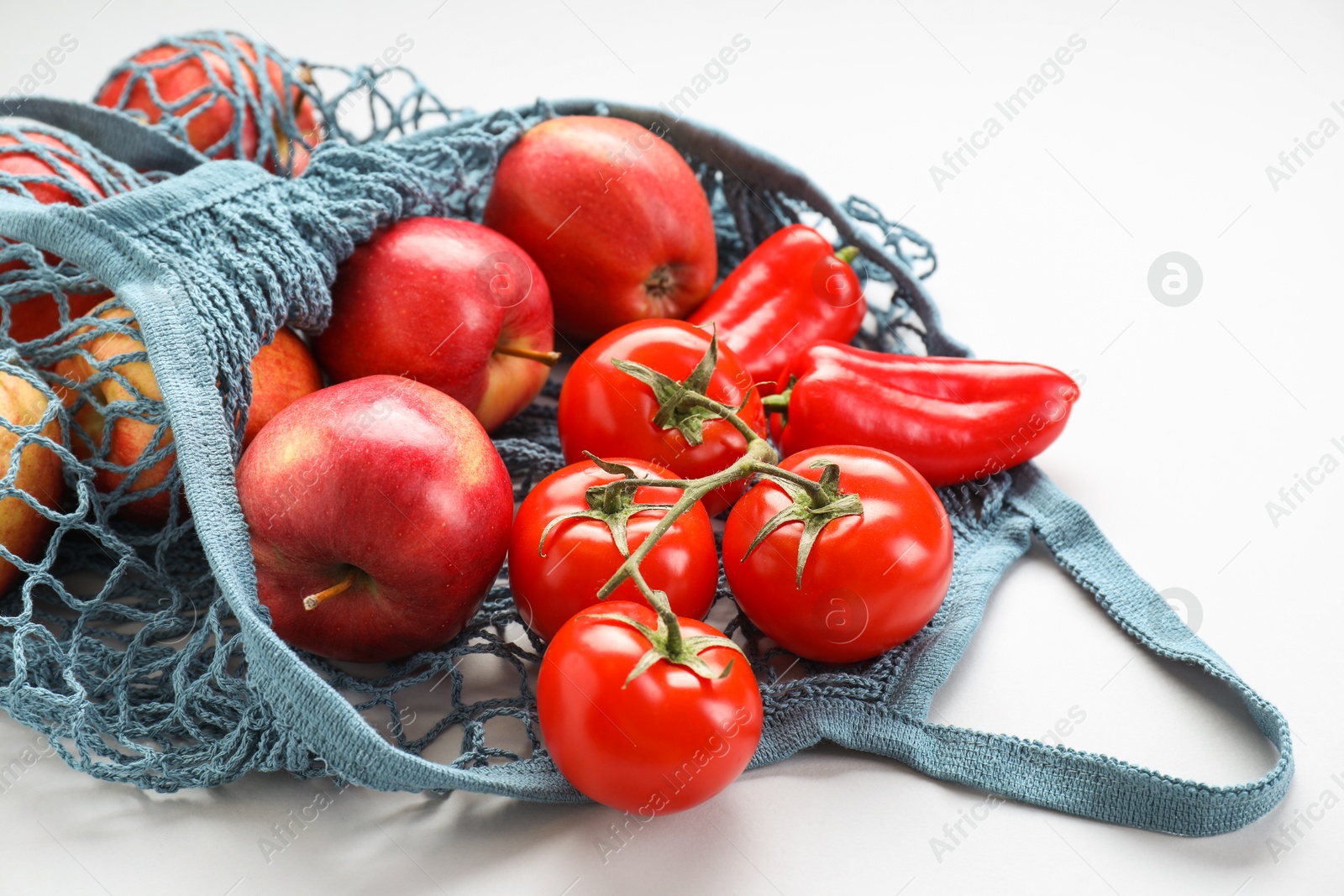 Photo of String bag with vegetables and apples on light grey background, closeup