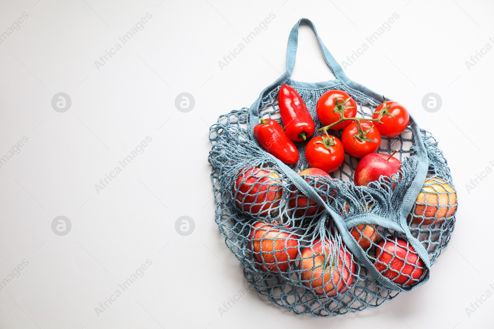 Photo of String bag with vegetables and apples on light grey background, top view. Space for text