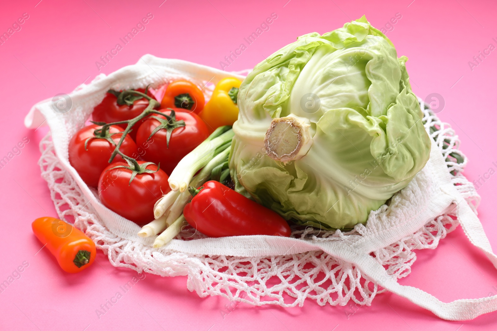 Photo of String bag with different vegetables on bright pink background, closeup