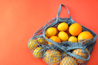 Photo of String bag with oranges and lemons on red background, top view. Space for text