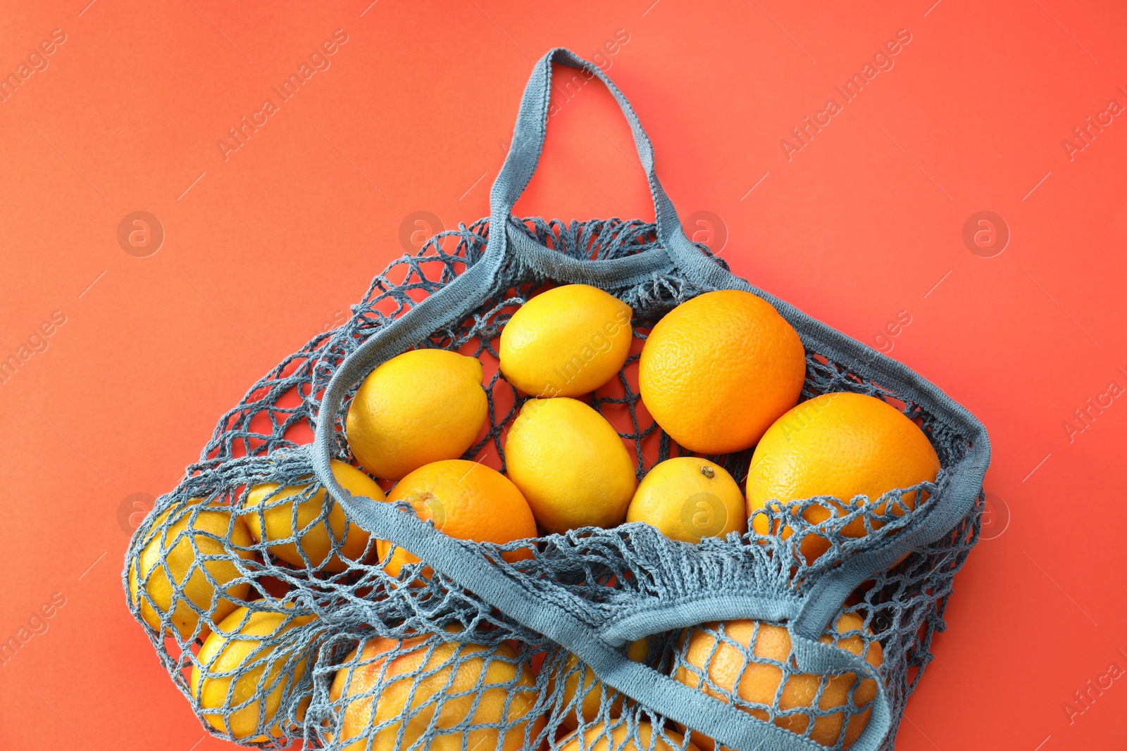 Photo of String bag with oranges and lemons on red background, top view