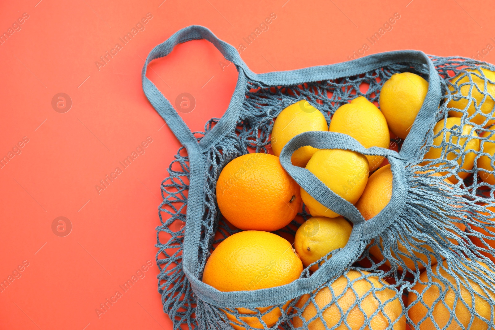 Photo of String bag with oranges and lemons on red background, top view. Space for text