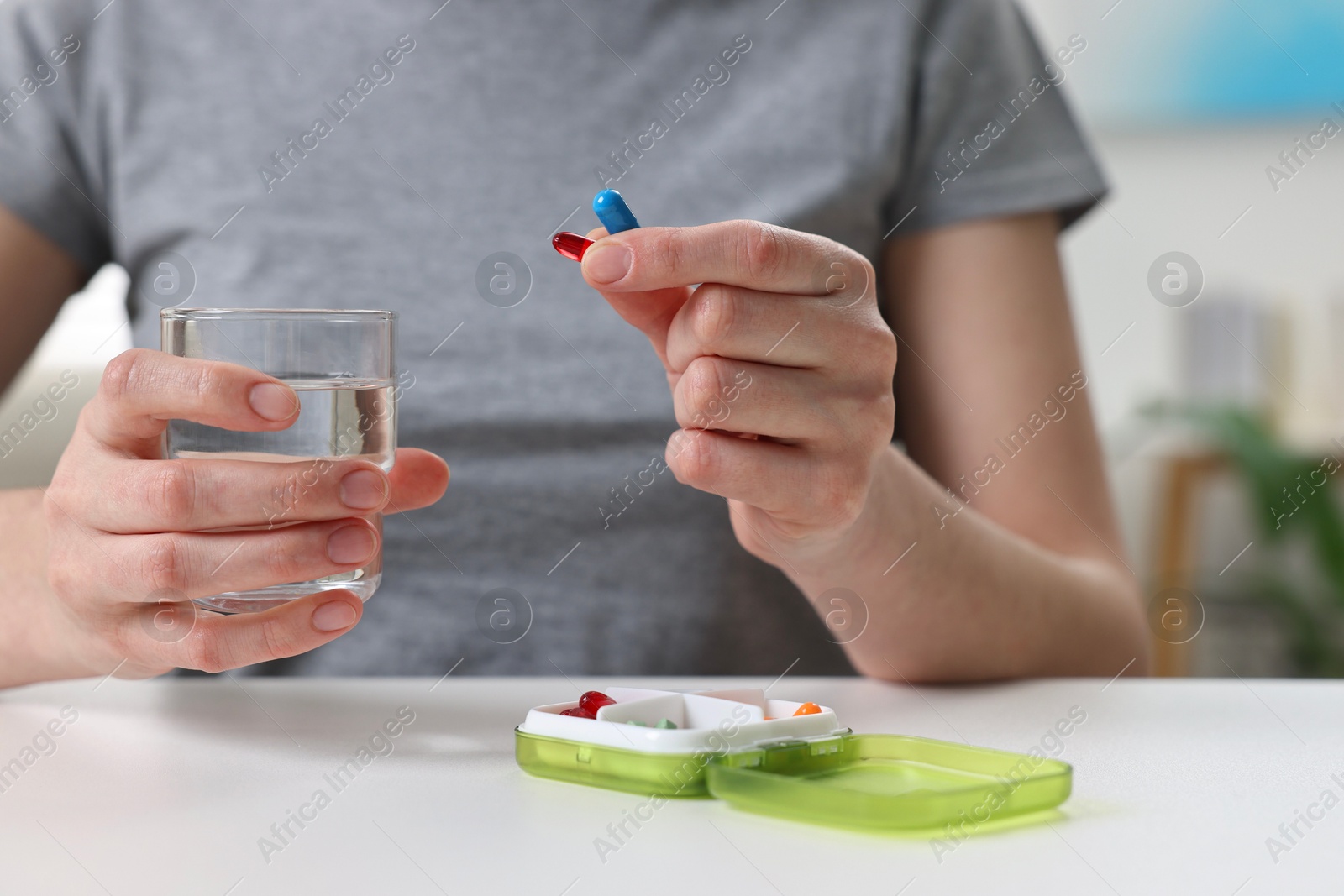 Photo of Woman with pills, organizer and glass of water at white table, closeup