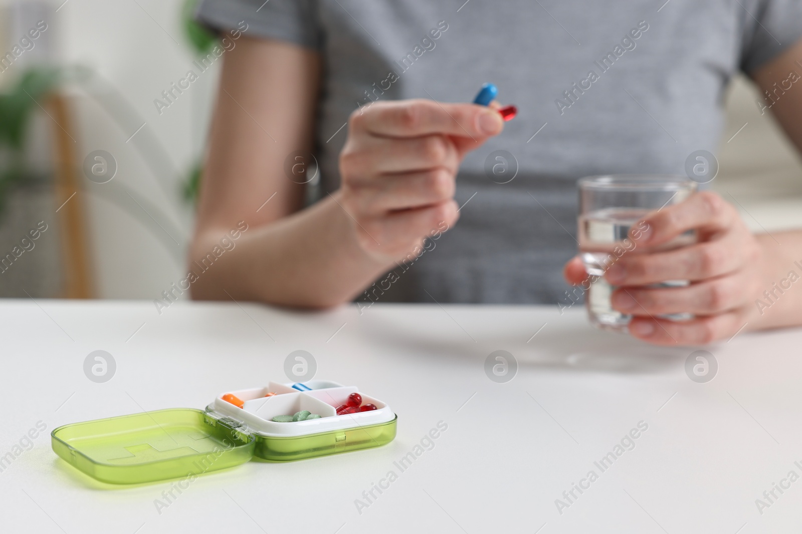 Photo of Woman with pills, organizer and glass of water at white table, selective focus